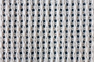 Close-up view of cotton canvas for hand cross stitch or other embroidery. Natural textile background of interwoven threads with square cells. Basis for needlework and hobby. Flat lay, macro, top view