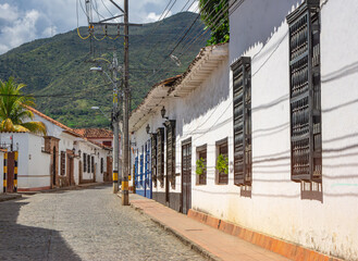Colonial style houses line a cobblestone street in Santa Fe de Antioquia, Colombia, with lush green...