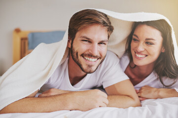 Smile, love and couple with blanket for relaxing, bonding and resting on bed together at home. Happy, romantic and young man and woman laying with duvet in bedroom at hotel, house or apartment.