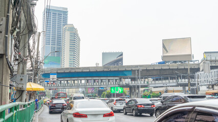 Fototapeta premium 1 January 2024 in Bangkok, Thailand Image of traffic starting to move through a red light intersection. At the top is a skywalk. Surrounded by many tall buildings.