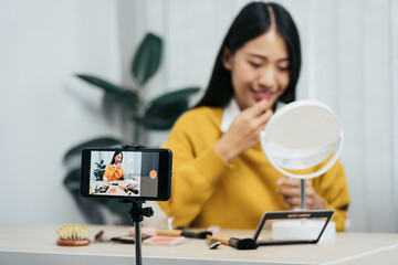 Young asian woman vlogging herself about beauty products with making a video for her blog on cosmetics using phone camera at home.