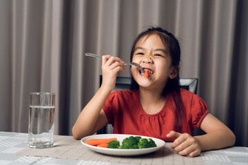 Asian little girl eating healthy vegetables with relish.