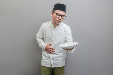 Asian Muslim man wearing a koko shirt and peci with shades of the fasting month, holding back...