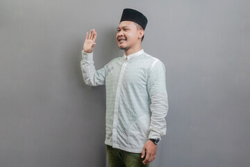 Happy asian muslim man waiving saying hello, friendly welcome gesture - obrazy, fototapety, plakaty