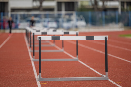 Hurdles for athletic running standing in a row. Open space on stadium, running track with a row of hurdles. Sunny day, person in bokeh in the background