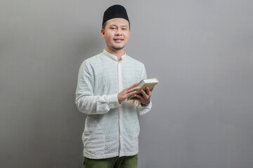 Asian Muslim man holding prayer beads and reading Qur'an