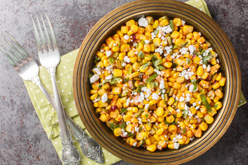 Mexican street corn snack Esquites with added sauce, chili, onion and cheese close-up in a plate on the table. Horizontal top view from above