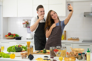 Young couple lover cooking together in the kitchen at home. Happy couple taking selfie with smartphone or making video call. - 763786022