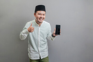 Portrait of an Asian Muslim man smiling with showing thumbs up and his smartphone