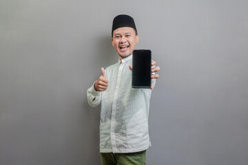 Portrait of an Asian Muslim man smiling with showing thumbs up and his smartphone