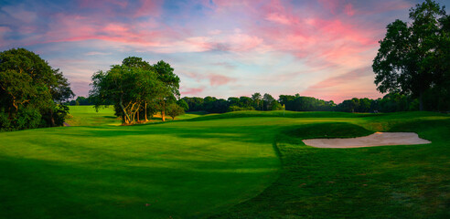 Panoramic landscape over the lush green fairway, the green, and the sand bunker at sunrise