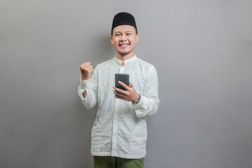 Asian Muslim man clenching his fist and holding his smartphone