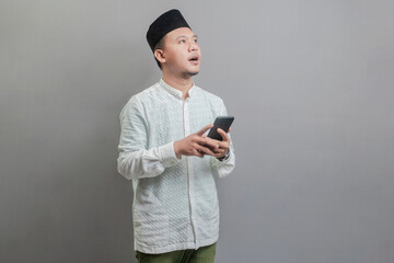 Asian Muslim man looking empty space and holding his smartphone
