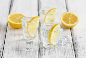 Shots of cold vodka with lemon on a white wooden table. Side view, selective focus. - 763792807