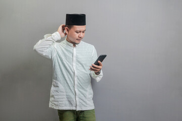 Asian Muslim man standing scratching his head and looking the smartphone