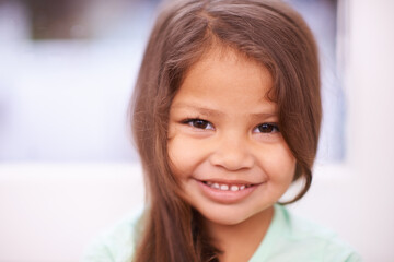 Naklejka premium Girl, kid and happiness for portrait in house, cute and sweet in lounge with smile in family home. Female young person, adorable and innocent in living room for child development, youth and childhood