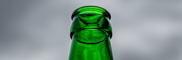 A striking low angle shot presents the bottleneck of an empty green beer bottle set against a...