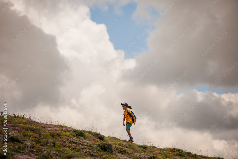 Sticker boy goes with a backpack against the backdrop of clouds in the mountains. child traveler with backpack, hiking, lifestyle concept