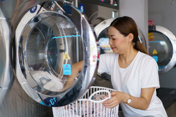 Asian female housewife bring used clothes to wash at self-service laundry shop.