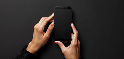 Close-up front view of a person's hands delicately holding a black screen mobile device with both hands against a backdrop of pure black