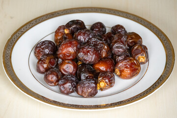 Delicious dried date palm fruits or kurma on a white plate on a wooden background. Locally in Bangladesh, it is called Khejur. Dates are high in fiber and antioxidants. 