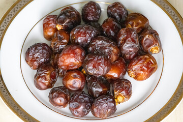 Sweet date palm fruits or kurma on a white plate on a wooden background. Locally in Bangladesh, it is called Khejur. 