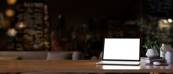 A white screen laptop computer on a wooden desk in a modern dark living room at night.