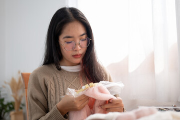 A focused young Asian woman threading a pattern on an embroidery frame, hand-sewing on cloth.