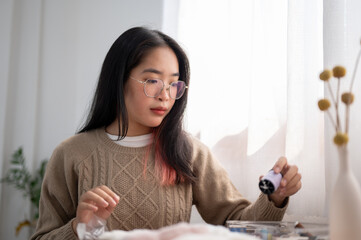 An Asian woman is threading at home, choosing a thread for her handcraft.