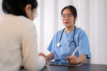 A professional Asian female doctor is working in her office, talking and giving advice to a patient.