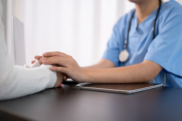 A doctor is touching a patient's hands on the table, comforting a patient during the consultation.