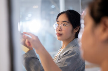 Obraz premium A businesswoman brainstorming and reading some ideas on sticky notes on a glass wall with her team.