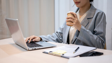 A hardworking businesswoman sipping coffee while working on her project on her laptop in her office.