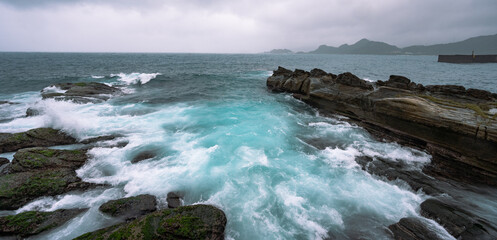 Windy day near the coast, ocean splashed hard on the rocks, and water color turn into light blue, in Keelung city, Taiwan.
