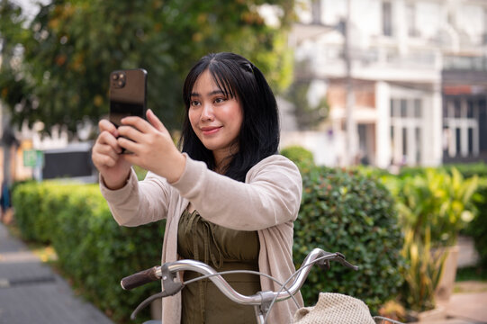 A woman is taking a picture of the city with her smartphone while exploring it with her bike.
