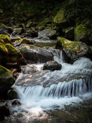 Beautiful river goes between rocks like a little waterfall, rocks full of green moss, and sunlight shines on it, in Nuandong Valley, Keelung city, Taiwan.