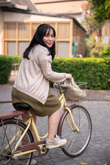 Obraz na płótnie Canvas A smiling, happy young Asian woman in a cute dress is riding a bicycle in the city
