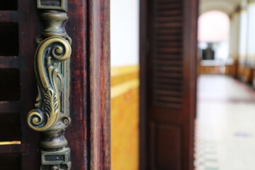 Old-style stainless door knob or handle made of steel on wooden door with louvre. handle made of...