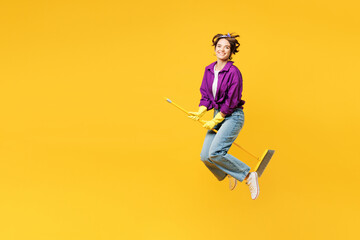 Full body young woman wears purple shirt casual clothes do housework tidy up jump high hold brush broom jump high pov fly like witch isolated on plain yellow background studio. Housekeeping concept. - obrazy, fototapety, plakaty