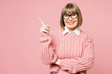Elderly smiling woman 50s years old wear sweater shirt casual clothes glasses point index finger aside on area mockup isolated on plain pastel light pink background studio portrait. Lifestyle concept. - 763829200