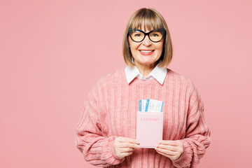 Traveler smiling happy elderly woman wear casual clothes hold passport ticket isolated on plain pink background. Tourist travel abroad in free spare time rest getaway. Air flight trip journey concept.