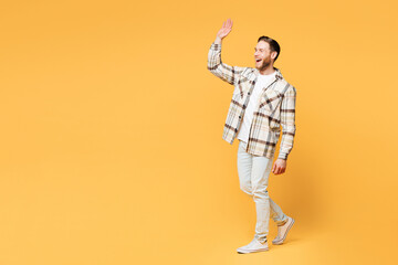 Fototapeta premium Full body side profile view young smiling happy Caucasian man he wear brown shirt casual clothes waving hand walking going isolated on plain yellow orange background studio portrait Lifestyle concept