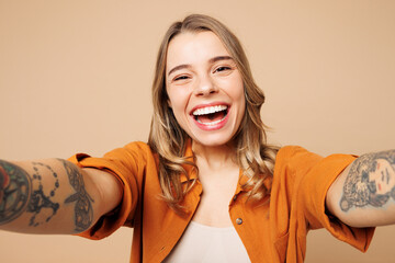 Close up young smiling happy woman wear orange shirt casual clothes doing selfie shot pov on mobile cell phone look camera isolated on plain pastel light beige background studio. Lifestyle concept