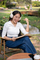 Obraz premium Happy Asian woman is listening to music, working or writing her diary while sitting in her backyard.