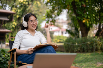 Fototapeta premium Happy Asian woman is listening to music, working or writing her diary while sitting in her backyard.