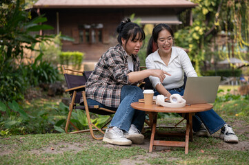 Two Asian female are talking and working on a project together while sitting at an outdoor table.