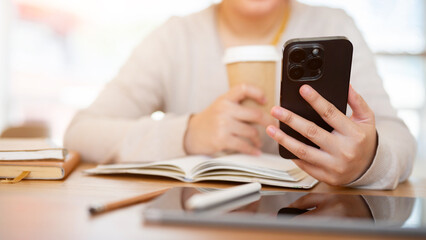 A cropped shot of a woman using her phone while working on her tasks at a table in a coffee shop.