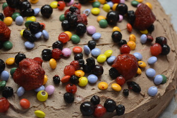 Bakery, homemade delicious pastries, sponge cake with brown cream sprinkled with bright colored candies with pieces of fruit.