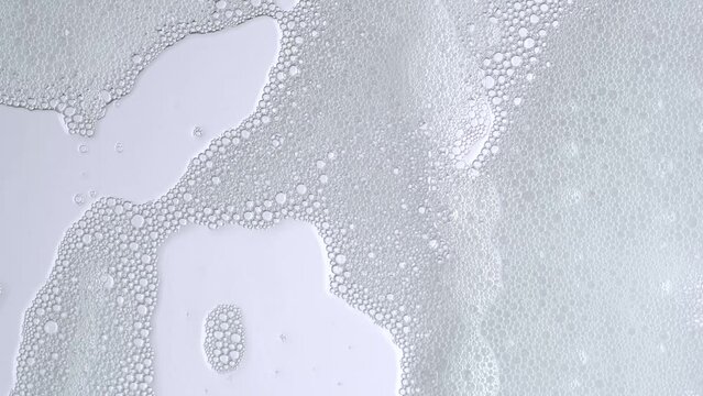 Soap bubbles on window glass. Macro shot of white soap suds flowing down of glass. Shower concept. Cleaning windows, hygiene, disinfection, housework, household, cleanup, washing.