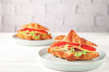 Fresh croissant with ham and lettuce on white wooden background